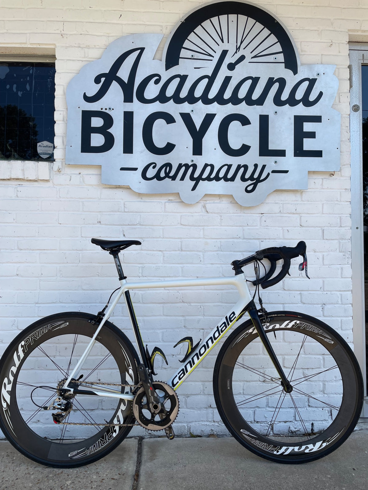 Used white Cannondale SuperSix EVO road bike with deep-section wheels photographed outside Acadiana Bicycle Company