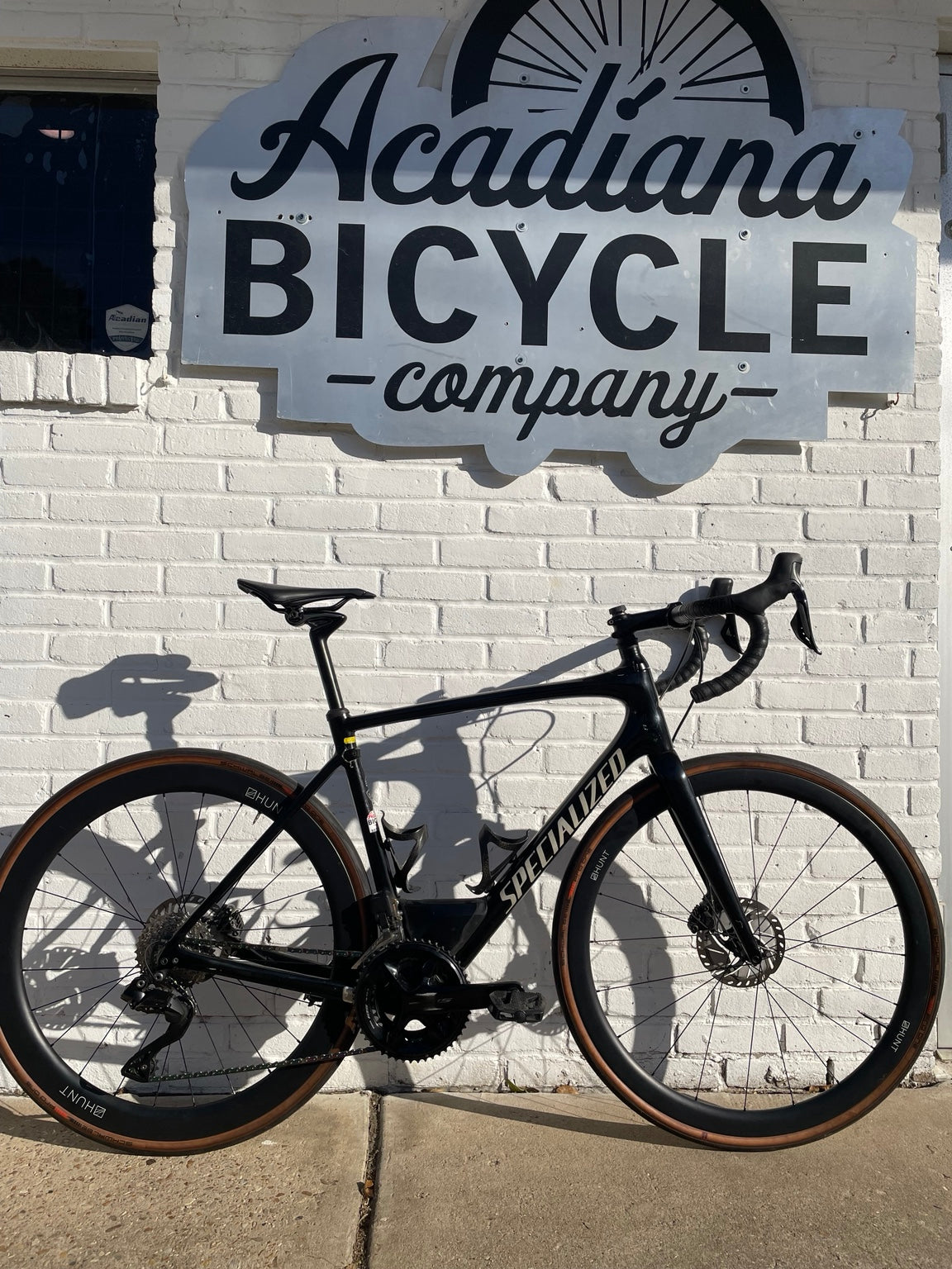 Black Specialized Roubaix carbon road bicycle with HUNT deep-section wheels outside Acadiana Bicycle Company